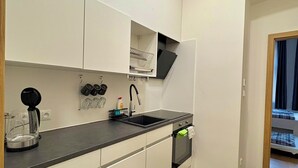Eine moderne Küche mit weißen Schränken, einer schwarzen Arbeitsplatte, einem eingebauten Backofen und einem kleinen Spülbecken.