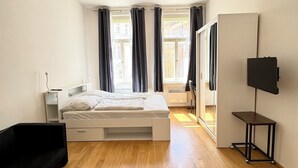 Ein Schlafzimmer mit einem Bett, einem kleinen Tisch, einem Fernseher und einem Fenster mit Vorhängen.