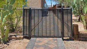 A gated entrance with a paved path leading to a building, surrounded by cacti.
