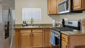 A kitchen with wooden cabinets, a stainless steel refrigerator, a microwave, and a stove.