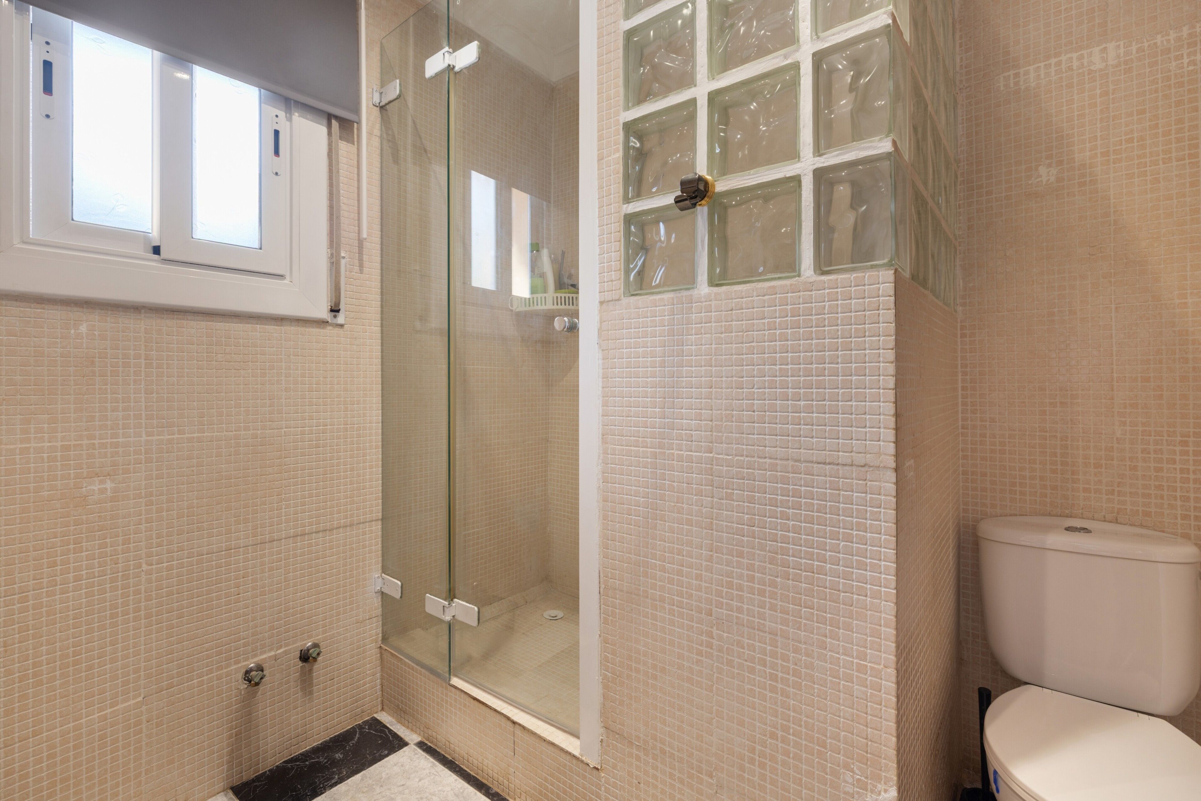 A bathroom with a glass shower enclosure, a toilet, and a window above the sink.