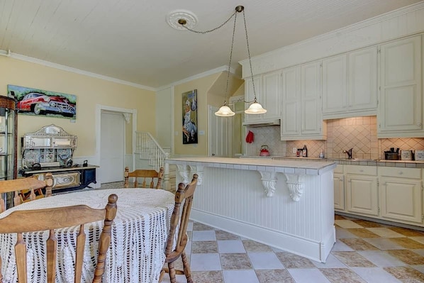 Une cuisine avec des meubles blancs, un îlot central, une table à manger avec des chaises et une machine à coudre ancienne.