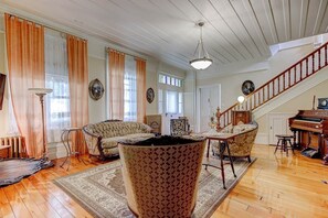 A spacious living room with a high ceiling, a grand piano, and a staircase.