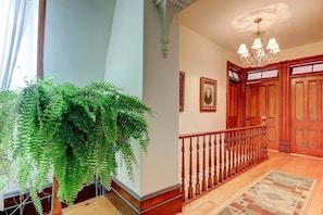 Un pasillo con una escalera de madera, un candelabro y una planta colgante grande.