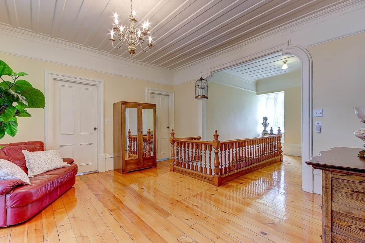 Une pièce spacieuse avec un plancher en bois, un canapé en cuir rouge, un escalier en bois et un lustre.