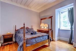 Une chambre à coucher avec un lit à baldaquin, une table de chevet, une commode, un miroir et une fenêtre avec des rideaux.