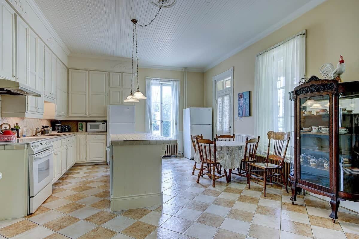A kitchen with white cabinets, a central island, a dining table with chairs, and a cabinet with glass doors.