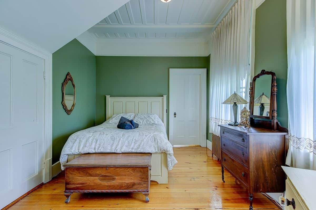 A bedroom with a wooden bed, a dresser, a mirror, and a door.
