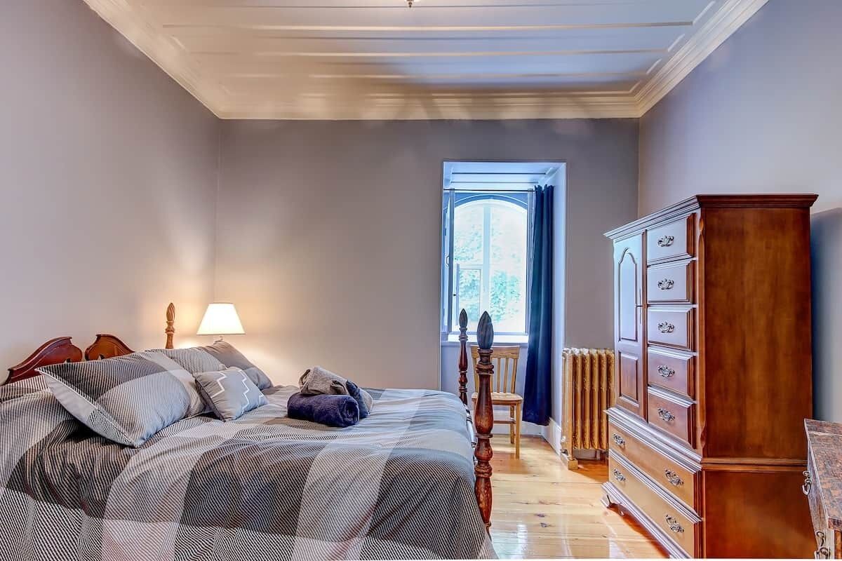 A bedroom with a bed, dresser, chair, lamp, and window.