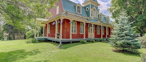 A large, two-story house with a prominent tower, a covered porch, and a well-maintained lawn.