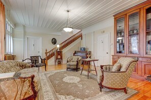 A spacious living room with a grand staircase, elegant furniture, and a large wooden cabinet.