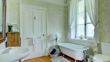 A bathroom with a white door, a freestanding bathtub, a sink, and a window with curtains.