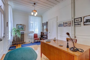Une pièce avec un bureau en bois, une chaise rouge, une plante et un radiateur.