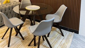 Moderni ruokailutila, jossa on pyöreä lasipöytä, neljä tuolia, napitettu sohva ja pystysuora puupaneliseinä.