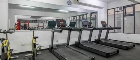 Un gimnasio con cintas de correr, bicicletas estáticas y máquinas de pesas.