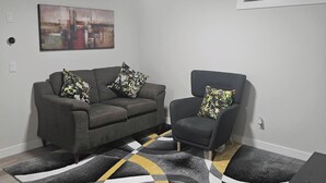 A living room with a sofa, armchair, and a patterned rug. - Brand new Cozy Basement Suite (Calgary)