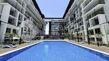 A modern hotel with a central swimming pool, multiple balconies, and a clear sky.