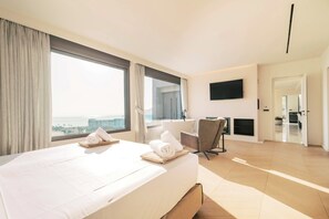 A hotel room with a large bed, a desk, a chair, a TV, and a view of the city.