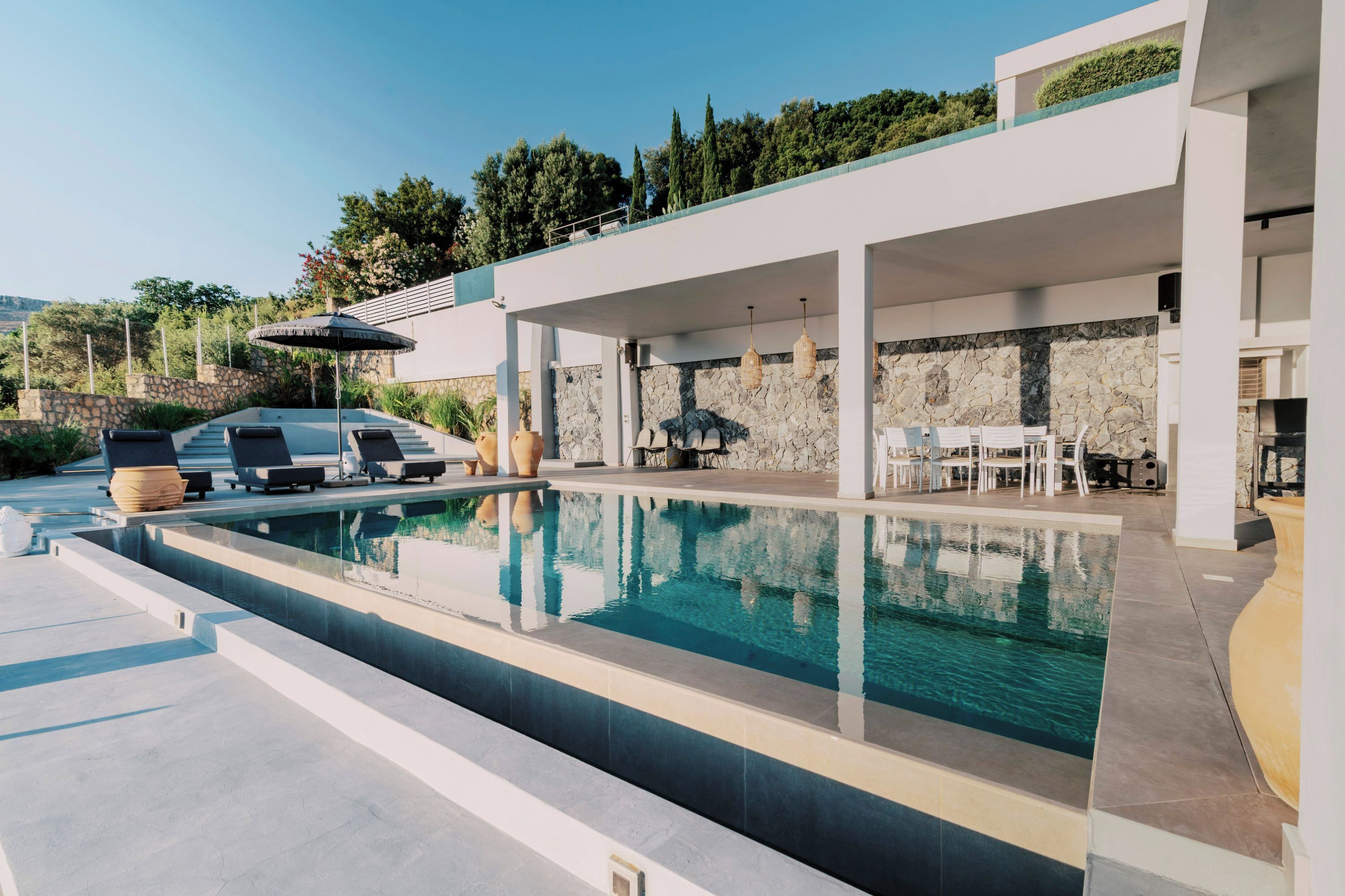 A modern outdoor pool area with lounge chairs, a dining area, and a stone wall.