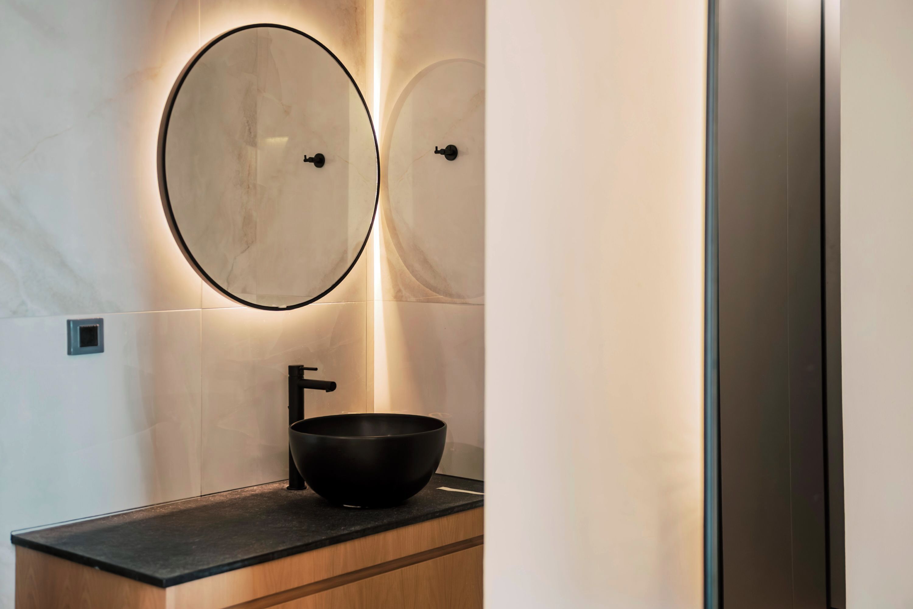 A modern bathroom with a black sink, two round mirrors, and a light fixture above the mirror.