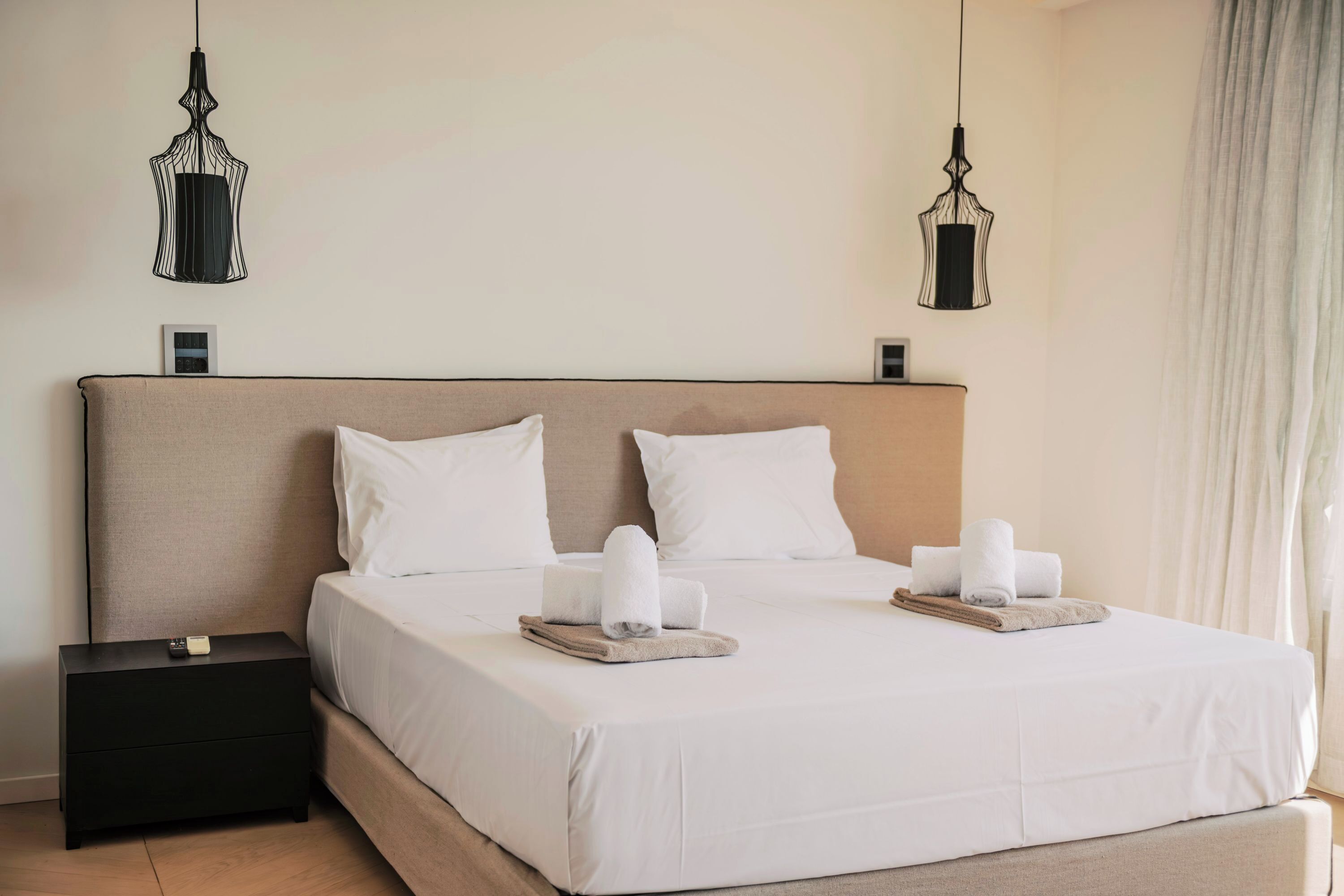 Een opgemaakt bed met witte lakens, twee nachtkastjes en twee hangende lampen.