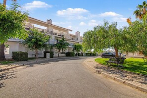 A residential street with a two-story building, a curved driveway, and a bench.