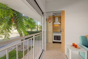 A balcony with a view of a tree and a paved area, leading to a kitchen with a stove and a hanging light fixture.