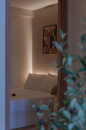 Ein Schlafzimmer mit Bett, Kissen, einem an der Wand hängenden abstrakten Kunstwerk und einer Pflanze im Vordergrund.