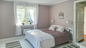 Un dormitorio con cama, ventana con cortinas, radiador y puerta.