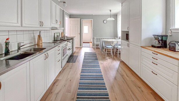Una cocina con armarios blancos, encimera de madera, estufa y comedor con mesa y sillas.