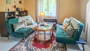 Una sala de estar con dos sofás color turquesa, una mesa de centro de madera, un tapete estampado y una ventana con cortinas.