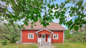 Una casa roja con puerta y ventanas blancas, rodeada de follaje.