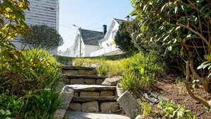 Una escalera de piedra conduce a un edificio blanco con techo negro, rodeado de follaje.