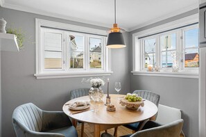 A dining area with a round table, chairs, a hanging light fixture, and windows with views of houses. - Charming and centrally located detached house by the marina. 3 bedroom, EV charg (Rogaland)