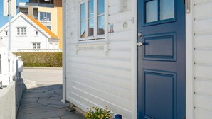 Un edificio blanco con puerta azul, un pequeño porche y una maceta.