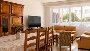 Uma sala de jantar com mesa, cadeiras, televisão e sofá.