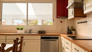 Uma cozinha com máquina de lavar louça, cadeiras de madeira, janela com vista e armários.