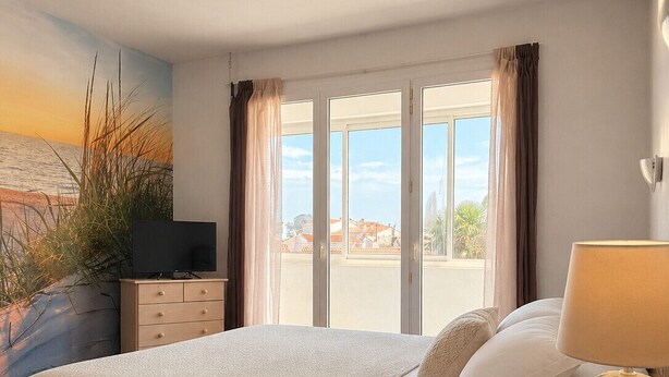 Quarto com cama, televisão, luminária e vista para o exterior.