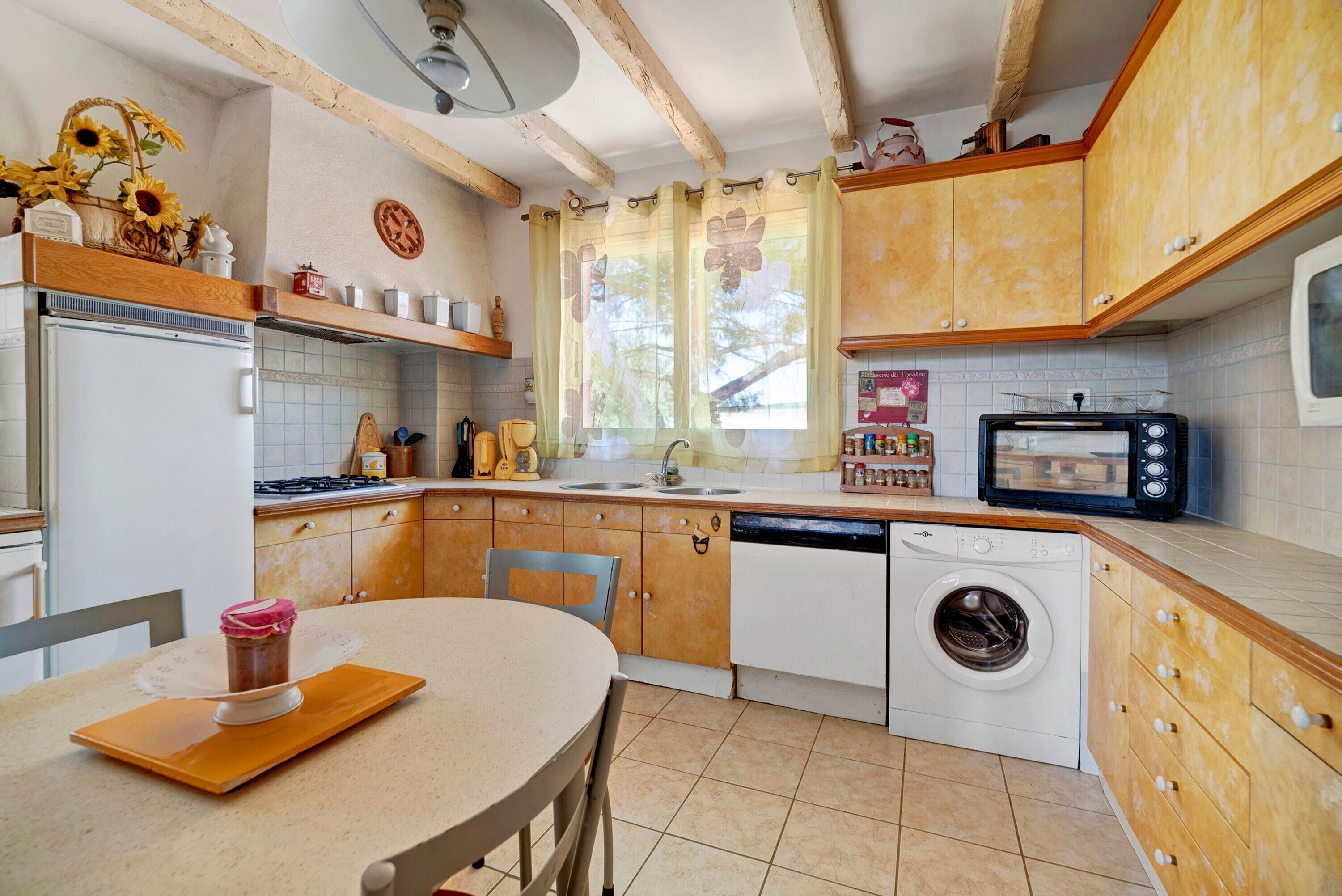 Une cuisine avec des meubles de rangement en bois, un lave-linge, une cuisinière et une table à manger avec des chaises.