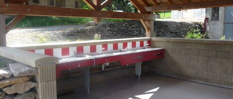An outdoor kitchen with a stone wall, a red and white counter, and a wooden ceiling structure.