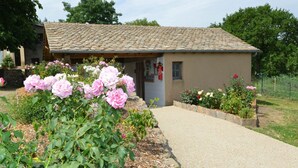 A small building with a tiled roof, surrounded by a garden with pink roses. - Bed and Breakfast 'Chambre La Paille' with Mountain View, Shared Pool and Wi-Fi (Castelnau-Pégayrols)