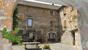 A stone building with a wooden door, a bench, and a planter with flowers. - Bed and Breakfast 'Chambre La Paille' with Mountain View, Shared Pool and Wi-Fi (Castelnau-Pégayrols)