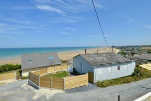 Een pand aan de kust met uitzicht op het strand, een omheinde tuin en een klein gebouw met een schuin dak.