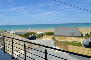 Blick auf die Küste mit Strand, einem Haus mit Schrägdach und einem geparkten Auto im Vordergrund.