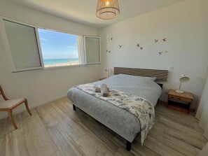 A bedroom with a bed, a chair, a bedside table with a lamp, a window with a beach view, and wall decals of birds. - L'Horizon, breathtaking views, right next to a bunker (Saint-Côme-de-Fresné)