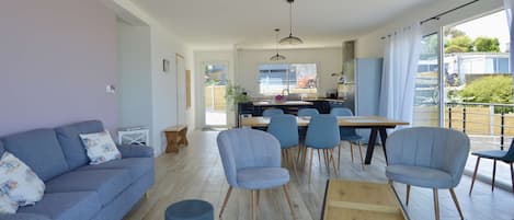 A modern living room with a sofa, chairs, a coffee table, and a dining area with a kitchen in the background.