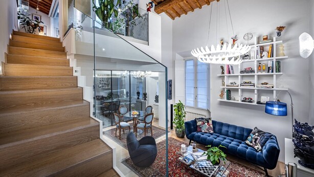 Un intérieur moderne avec un escalier, un salon doté d’un canapé bleu et une rambarde en verre.