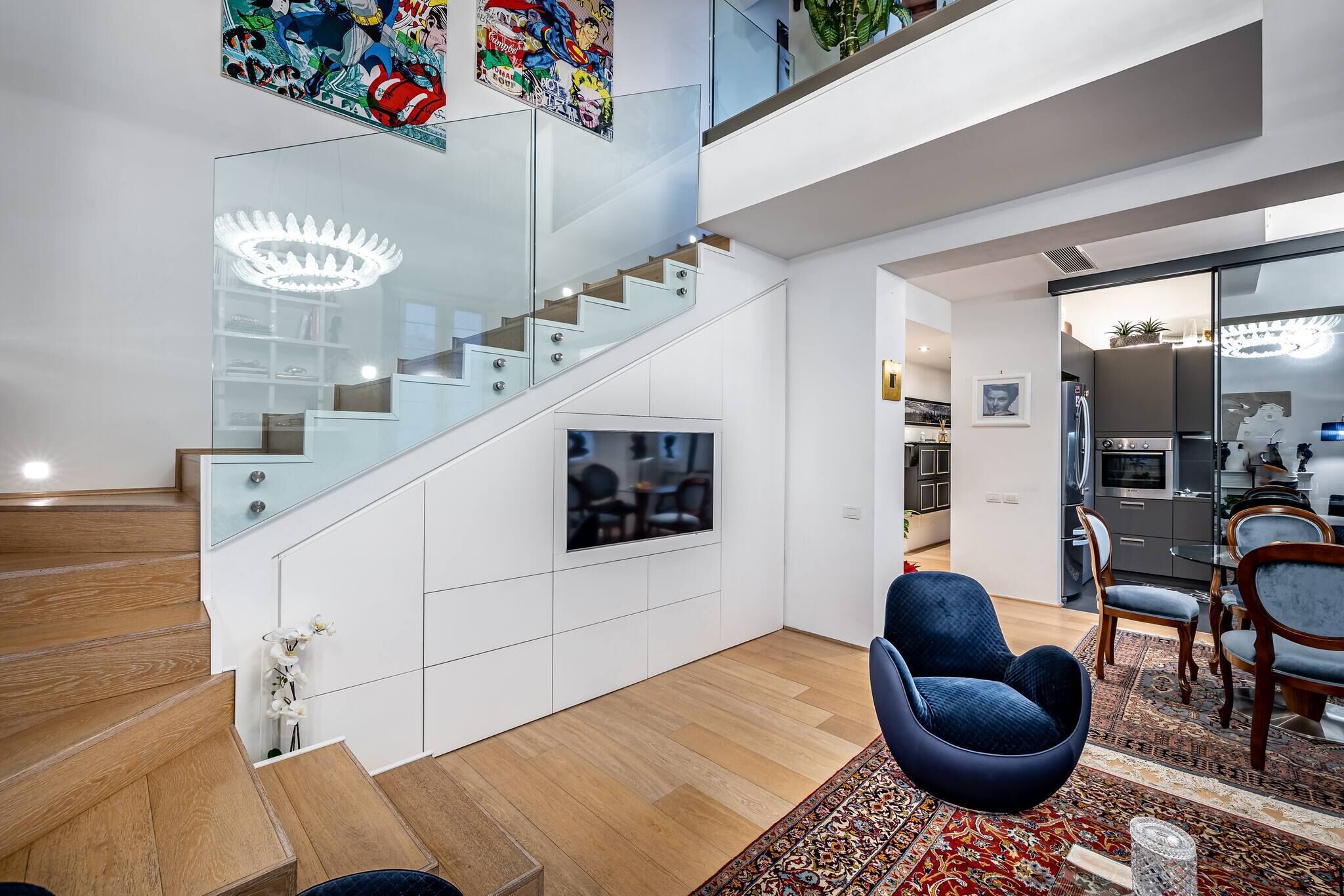 A modern interior with a staircase, a dining area with chairs, and a kitchen visible through an open door.