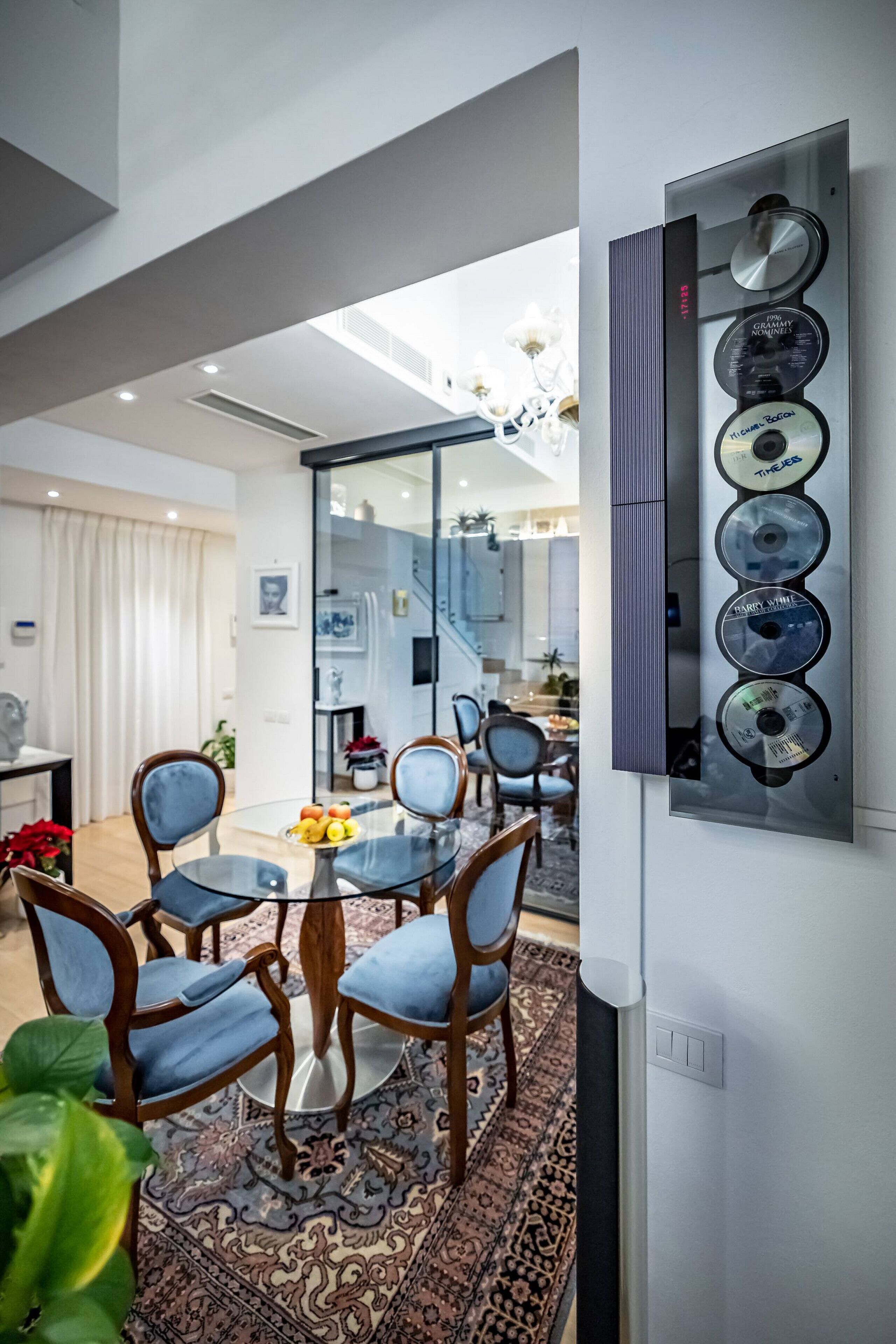 A modern dining area with a glass table, blue upholstered chairs, and a patterned rug.