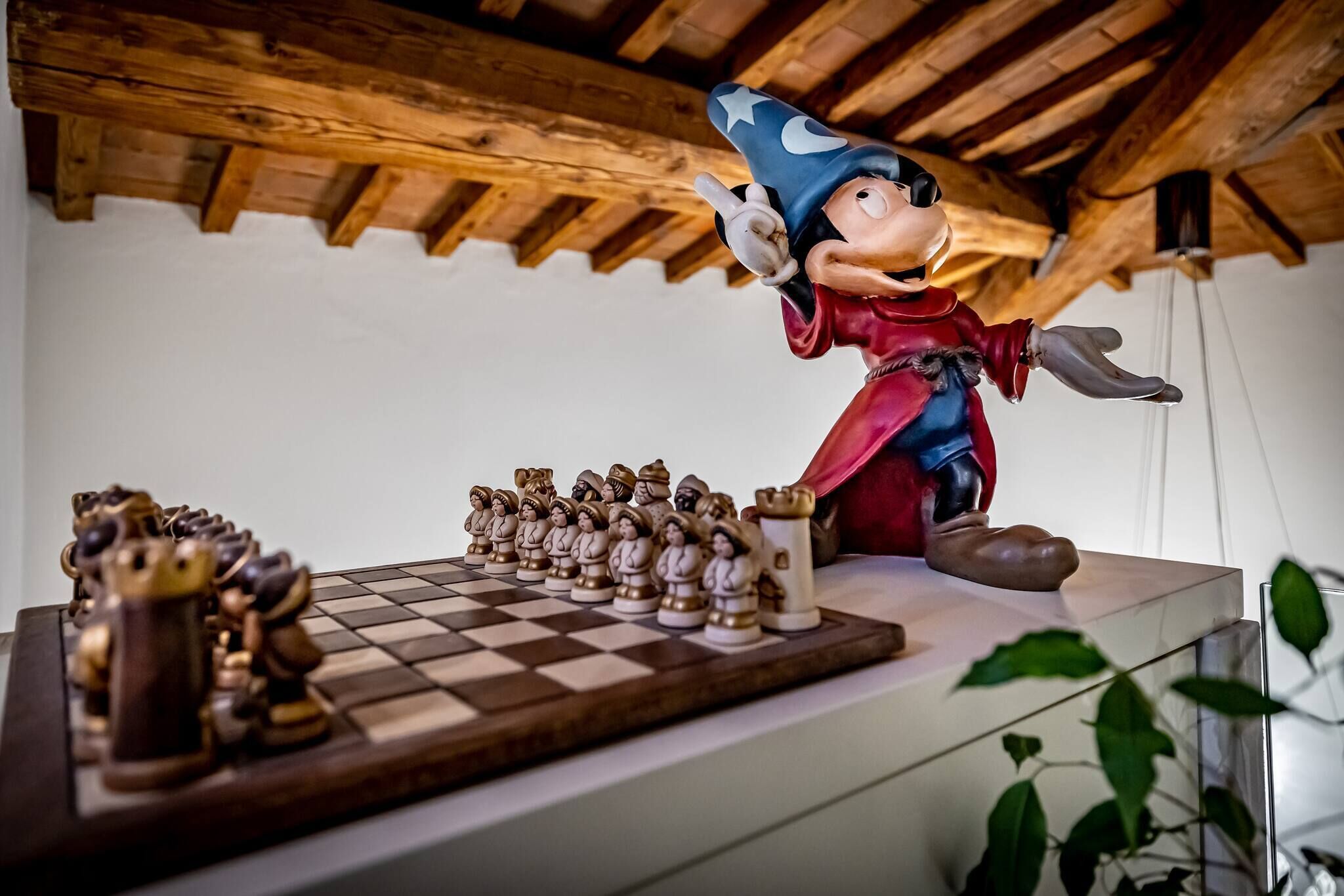 A wooden ceiling with exposed beams, a chessboard with wooden pieces, and a figurine of a character in a red coat and blue hat.